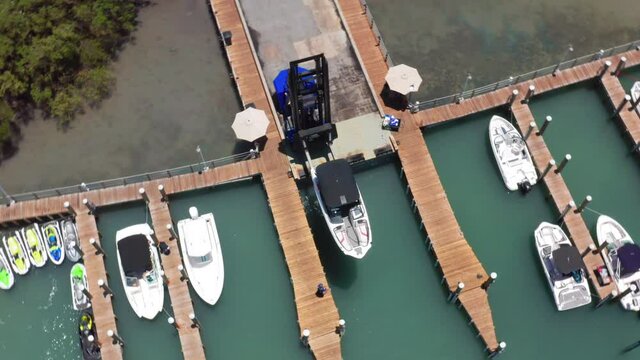 Circular drone view of boat loader slowly launching the white yacht from the pier in the Miami harbor. The boat launch ramp in the marine port. Beautiful 4K aerial video of water transportation, USA