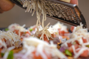 slicing cheese cubes using cheese grater or slicer on top of delicious mini pizzas