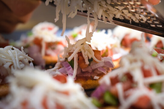 slicing cheese cube using cheese grater or slicer on top of mini baked pizzas