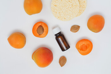 apricot oil bottle with ripe apricots, apricot kernels and face sponges isolated white. Top view