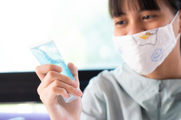 Girl Wearing Cotton Face Mask Using Hands Sanitizer Alcohol Gel or Anti-Bacterial Hand Gel to Clean Her Hand and Protect Hands From Touching Dirty Surfaces.  Corona Virus, COVID-19 Concept.