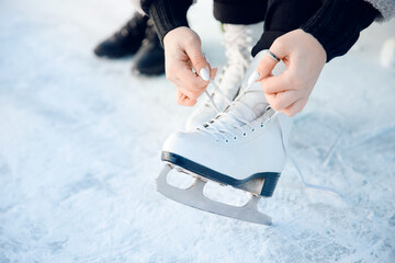 Girl ties shoelaces on white figure skates for ice rink in winter. Christmas holidays concept