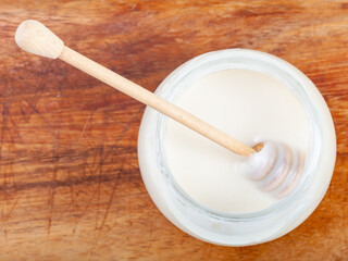 top view of wooden stick in glass jar with natural organic white honey on wooden board