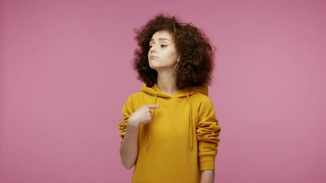 I'm the best! Selfish haughty girl afro hairstyle in hoodie pointing herself, looking at camera with arrogance superiority, bragging own success. indoor studio shot isolated on pink background