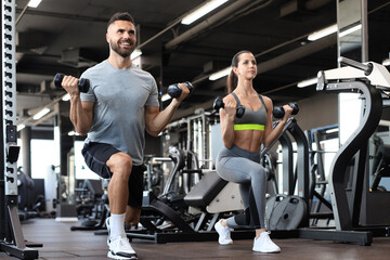 Fototapeta na wymiar Attractive sports people are working out with dumbbells at gym.