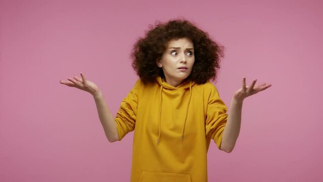 What do you want? Confused girl afro hairstyle in hoodie gesturing in puzzlement, looking inquiring with raised hands, asking why, misunderstanding in conflict. studio shot isolated on pink background
