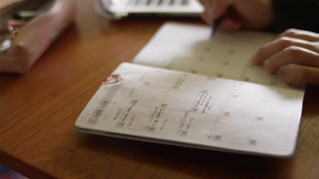 Writing in a planner calendar on a desk with shallow focus