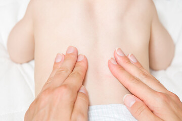 Young mother fingers doing massage on baby back. Lying down on bed. Body health problem. Closeup. Point of view shot.