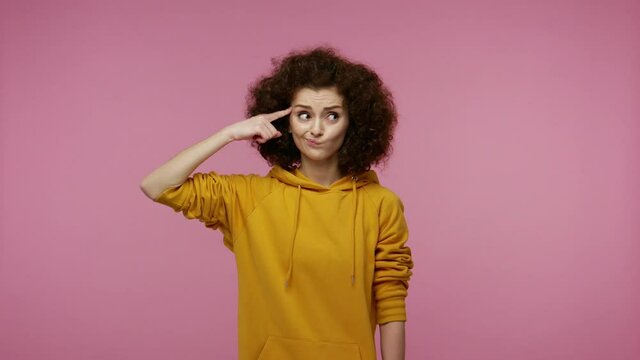 Displeased annoyed girl afro hairstyle in hoodie showing stupid gesture, accusing crazy cuckoo mind, blaming insane idea, reckless plan, senseless dumb talk. studio shot isolated on pink background