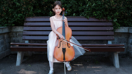 beautiful girl in a pink dress sits on a bench with a cello © Fotograf