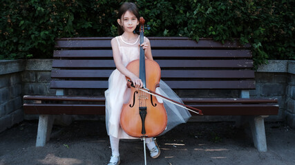 beautiful girl in a pink dress sits on a bench with a cello