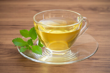 Close up cup glass of Stevia tea with fresh organic stevia rebaudiana leaves isolated on wood table background. Sweetener plant, herbal medicinal diet concept.
