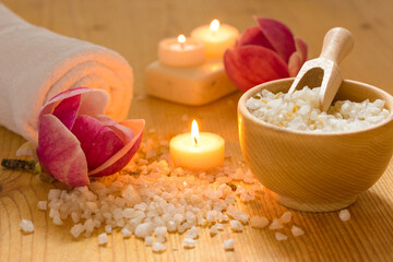 Spa set still life with aromatic candles, spa salt, white bath towel and beautiful flowers. Warm atmosphere.