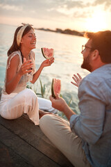 young couple sitting by the water talking, smiling, eating watermelon