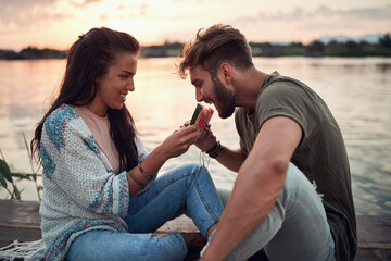 young woman feeding man with slice of watermelon by the river