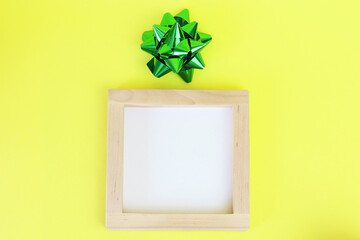 Wooden frame and green bow. Colorful, yellow background for text. Copy space - holidays concept, gift, place for congratulations.