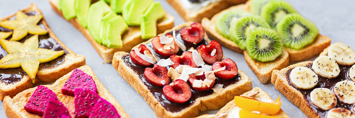 Sandwiches with cream cheese, chocolate, fresh fruits and berries on a gray concrete background. Horizontal web banner. top view. Flat lay. Healthy diet