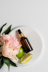 Glass brown bottle with serum and a pipette for skin care on a light background with peony flowers and lime. The concept of health and beauty. minimalism