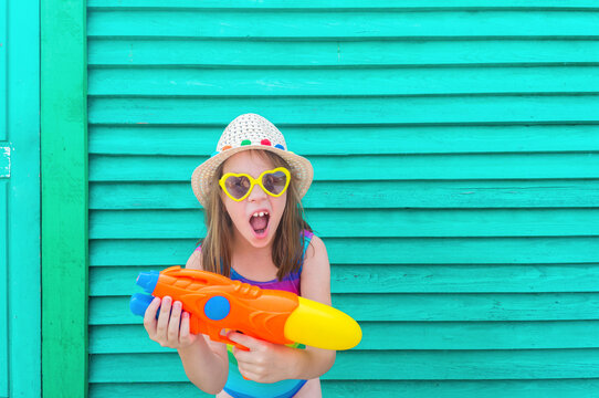 Girl with a water gun. Baby in hat and glasses on a wooden background.