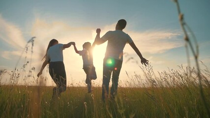 A happy family runs through the green grass in the Park holding hands at sunset. Happy child, running children in the countryside. Teamwork. - Powered by Adobe