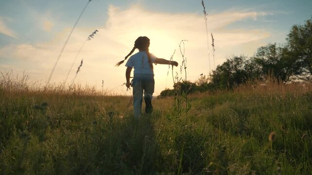 A healthy, happy, carefree child runs along a green summer field, enjoying nature, fresh air, moving towards goal, dream. happy family. A girl at sunset on a summer day.