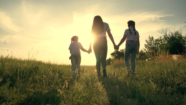 Happy family.A young mother walks with her children in a field at sunset. Two cute girls hold the hand of their mother, sister, teacher