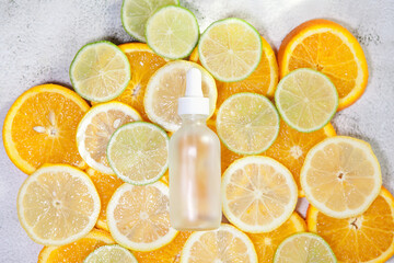 Cosmetic bottle made of transparent glass with pipette on fresh lemon, orange, lime slices background. Copy space.
