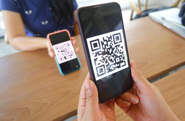 Women's hand uses a mobile phone application to scan QR codes in stores that accept digital...