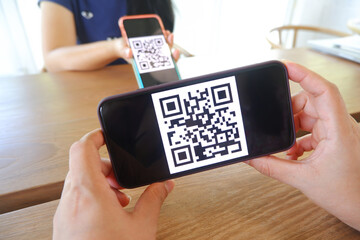 Women's hand uses a mobile phone application to scan QR codes in stores that accept digital...