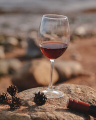 Red wine glass with bottle on the rocky sand. Summertime, vacation, weekend on Baltic sea, pine trees, northern nature