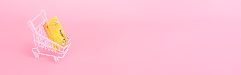 shopping and payment concept from small trolley and credit card on pink pastel color background....