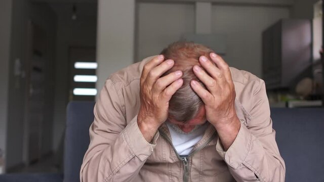 Problems of unemployment and the economic crisis. A sad gray-haired man sits on the couch and covered his face with his hands