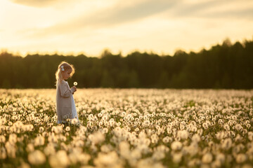 A little girl with blond hair in a white dress is picking flowers in a huge endless field of white...