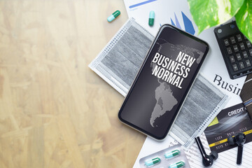 The Business New Normal After Covid-19 background concept. A smartphone with new business normal message with world map, medical face mask, medicine tablet  on businessman working desk.