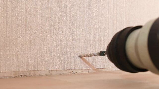 Close up human hands with electric drill making hole in white concrete wall at home
