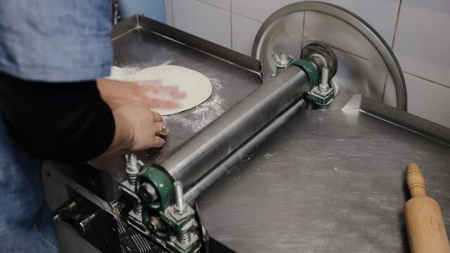 Chef making dough pastry sheeter at the kitchen. Baker forming shaping dough rolled pastry metal work table closeup hands process of preparing bread khinkali dough roller machine thin pasta sheet