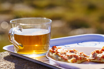 Tea mug and pizza slices on plate, outdoors