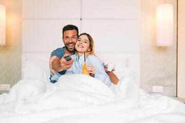 Couple hugging and holding drinks while watching TV in a hotel room