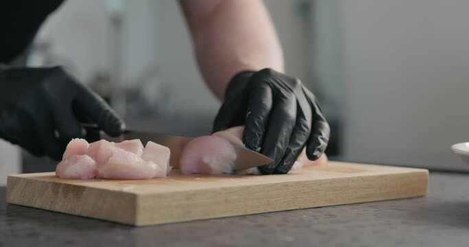 Slow motion man in black gloves slicing chicken fillet on oak cutting board