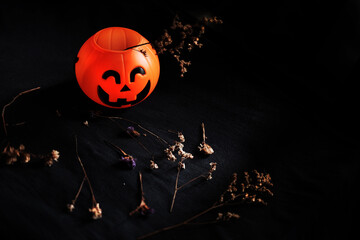 Halloween pumpkin head with dry flowers on black clothes in natural shadow and light. Halloween holiday concept.