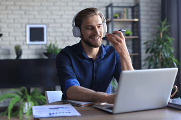 Satisfied business man in glasses holding smartphone near mouth for recording voice message or...
