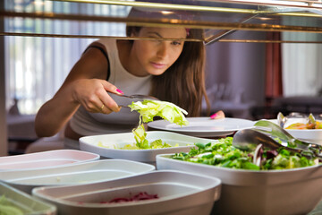 Woman with a turban picking up salad with a clip from a display case