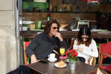 Couple of good friends met by chance in the street sat sidewalk cafe at cool autumn day  happily discuss all the latest news in their lives while they enjoying cup of coffee and fresh juice breakfast