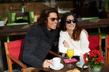 Young happy caucasian couple enjoying good day while they breakfast together in coffee shop,two enamored people spending time together while embrace in love,smiling handsome man hugging his girlfriend