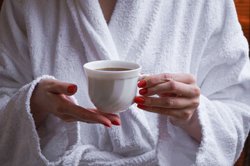 The concept of rest in a hotel. A cup in the hands of a girl in a white coat.