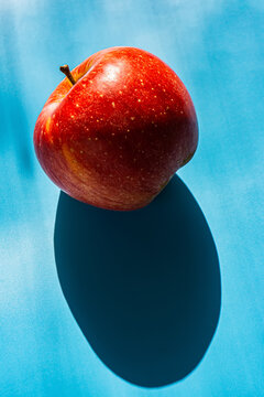 Red apple and shadow lies on a blue background.