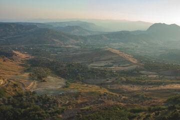 Panoramic aerial view of a italian valley from above, it is possible see trees and wood, with some road and mountain in background. Sunset moment