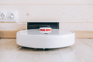 Wireless robot vacuum cleaner return to charging at dock in clean wooden floor.
