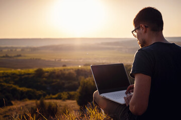 man with laptop sitting on the edge of a mountain with stunning views of the valley