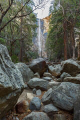 View of the winter Bridalveil Fall, trees, huge river rocks and Tuolumne River in Yosemite Park, California.